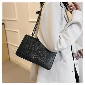 Close-up of snake skin texture flap bag with black chain strap on white blazer