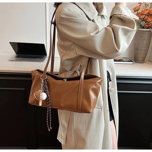 Detail view of brown glossy tote bag with leather straps and baseball charm