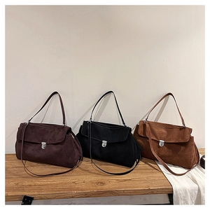 Three suede underarm bags in brown, black, and camel displayed on a wooden bench