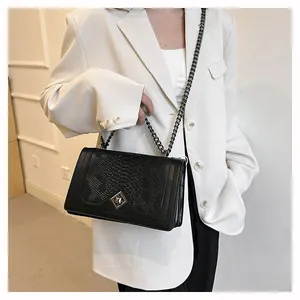 Detail of snake pattern leather flap and dark grey metal chain on a black crossbody bag