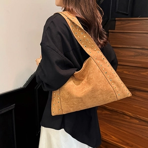 Brown suede shoulder bag with gold metal eyelets shown on a wooden staircase