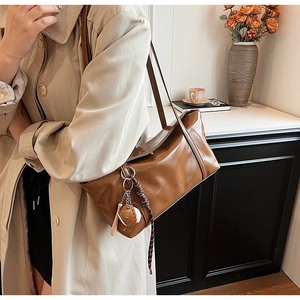 Detail of glossy brown leather shoulder bag with creative ball-shaped charm pendant