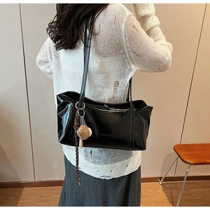 Close-up of black glossy oil wax leather tote bag with embossed letters and baseball charm