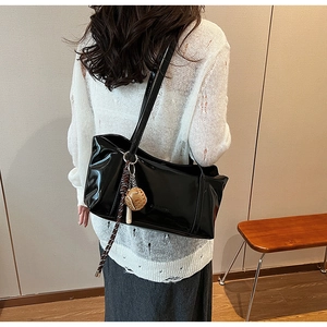 Close-up of black patent leather tote bag with baseball glove pendant and fringe detail