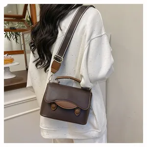 Détail d'un sac bandoulière en cuir grainé marron foncé avec large sangle tissée