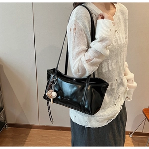 Detail of black faux leather tote with heart charm on shoulder of a model