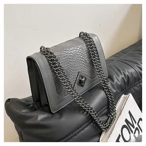 Detail of grey snakeskin flap bag with silver chain strap on leather surface