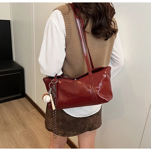 Detail of burgundy glossy leather tote bag with baseball charm and embossed design