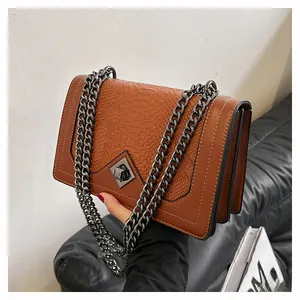 Detail of brown faux snake skin leather handbag with metal chain strap and geometric lock