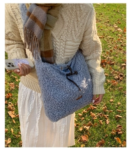Detail of light blue faux shearling tote bag with drawstring and leather tag in outdoor setting