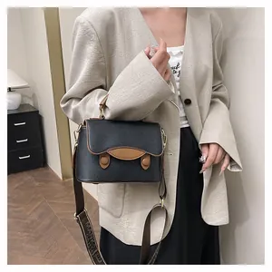 Détail d'un sac à bandoulière noir vintage avec bordure marron et sangle tissée large