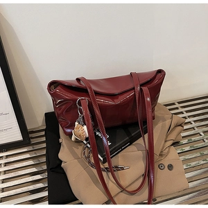 Detail of burgundy glossy tote bag with baseball pendant on metal bench