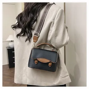 Détail du sac bandoulière en cuir grainé noir avec bordure brune et sangle tissée