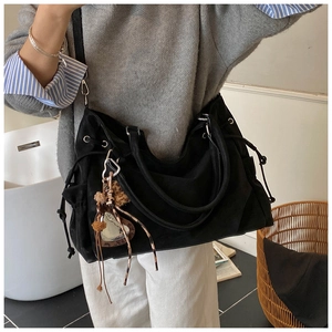 Detail of black large canvas tote bag featuring side drawstring pocket and metal heart charms