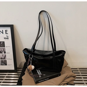 Detail of glossy black faux leather tote bag with unique baseball glove charm accessory