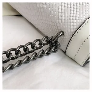 Detailed macro view of white snakeskin texture and gunmetal chain on a small square bag