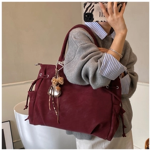 Detail of burgundy suede tote bag featuring side drawstrings and leopard faux fur pompom