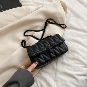 Elegant black quilted chain bag with circular lock on a stylish blazer background