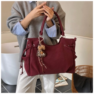 Detail of burgundy tote bag featuring side pocket, metal rings and leopard heart charm