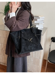 Detail of black leather tote bag featuring cross-strap design and gold metal buckle