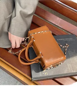 Detail shot of a caramel brown leather tote bag with a golden chain strap on a book