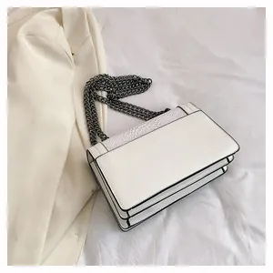 Detail of white leather shoulder bag with snake skin texture and gray metal chain strap