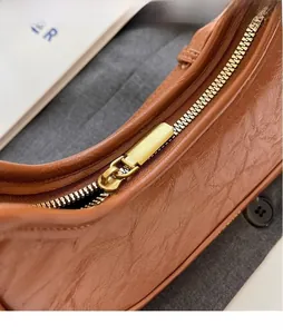 Detailed close-up of brown oiled leather crescent bag featuring a golden metal zipper