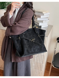 Close-up of black leather tote bag with gold metal buckles and wide shoulder strap