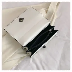 Detail of white faux leather flap bag featuring black diamond lock and accordion structure