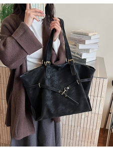 Detail of a large black tote bag featuring a crisscross leather strap and gold buckle
