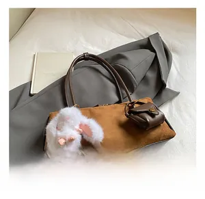 Nahaufnahme der braunen Wildleder-Schultertasche mit einem weißen Plüsch-Hasen-Anhänger