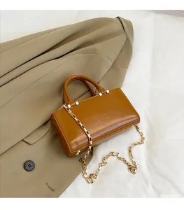 Detail of a brown leather shoulder bag featuring a golden chain strap and top handle