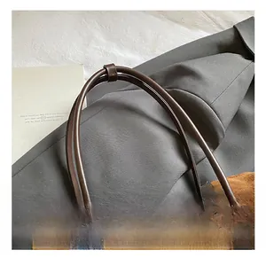 Detail einer braunen Wildleder-Schultertasche mit Lederriemen und Plüsch-Pompon-Anhänger