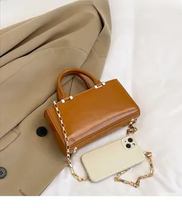 Flat lay of brown rectangular handbag with gold chain strap on khaki blazer background