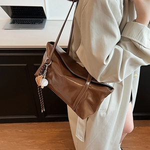 Retro brown glossy large tote bag with baseball charm shown on shoulder with beige trench coat