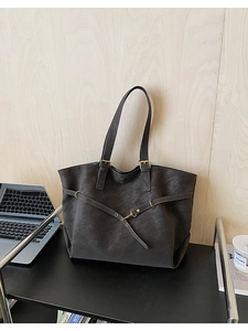 Detail of charcoal black tote bag showing leather texture and metal buckle on desk