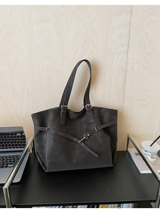 Detail view of large charcoal grey leather tote bag with metal buckles on wooden shelf