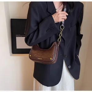 Detail of deep brown crescent bag featuring pleated leather texture and gold chain strap
