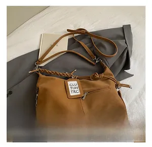 Détail du sac hobo en cuir marron avec bandoulière tressée et étiquette décorative
