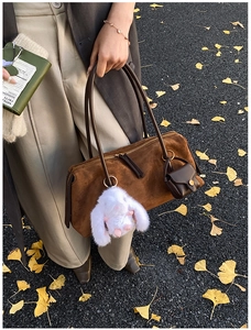 Details einer braunen Wildleder-Boston-Tasche mit Hasenanhänger auf herbstlichem Laub