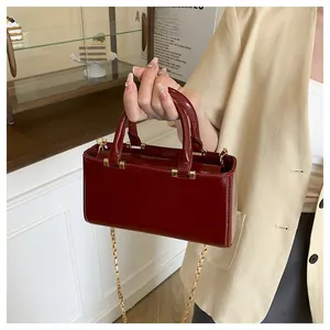 Detail of burgundy patent leather square bag with gold chain strap and dual handles