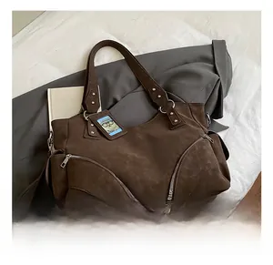 Close-up of brown suede tote bag with decorative silver zippers and bear charm
