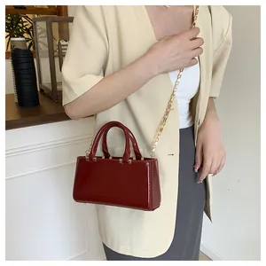 Detail of burgundy patent leather tote bag with gold chain strap on a female model