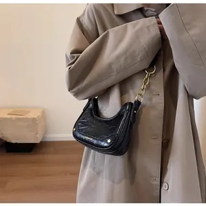 Close-up of black crescent hobo bag featuring glossy crinkled leather and gold chain detail