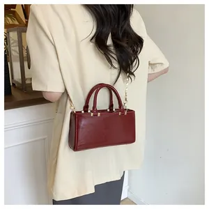 Detail of burgundy glossy leather tote bag with gold chain strap on model outfit