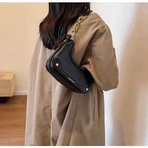 Detail of a black moon-shaped hobo bag with gold studs and chain on a stylish trench coat
