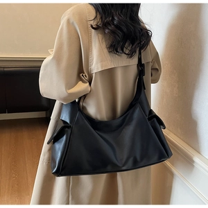 Detail of a black matte leather tote bag featuring a functional side flap pocket and wide strap