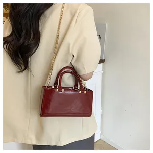 Detail of burgundy leather crossbody bag with gold chain strap and metal rivet accents
