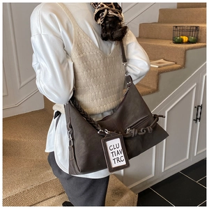 Detail of brown faux leather hobo bag with thick woven strap and modern logo tag