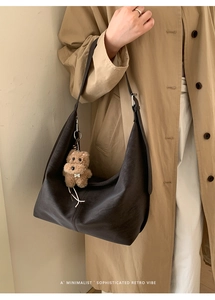 Detailed close-up of dark brown textured leather hobo bag with a plush bear charm